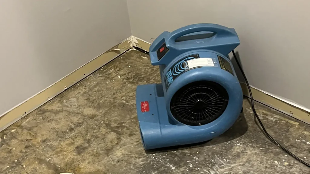 Air mover drying a wet corner and flooring where the baseboard has been removed.