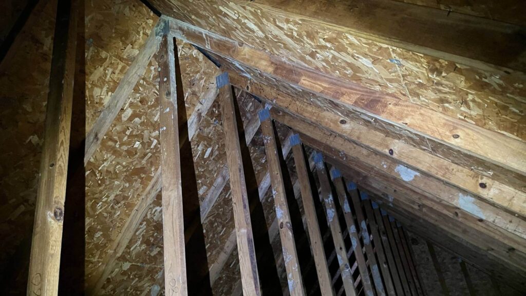 View of a dimly lit attic showcasing wooden beams and osb sheathing, revealing the structural framework of the roof.