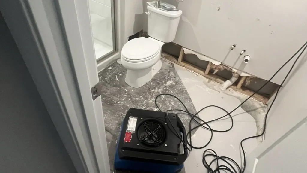 Water damage restoration from a flooded toilet with damaged drywall removed and exposed floor for drying.