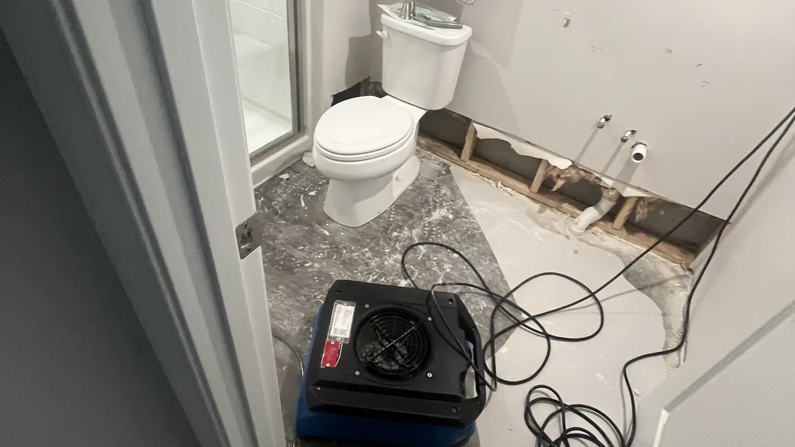 Bathroom with a toilet and a vacuum cleaner, showing signs of water damage on the walls and floor.