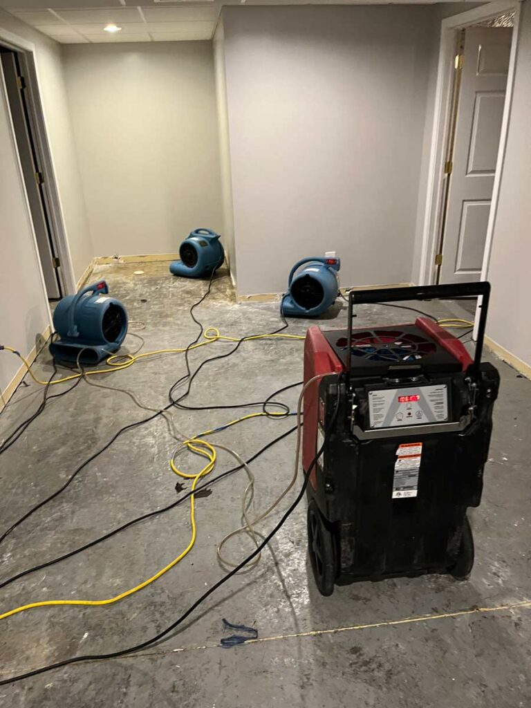 A partially finished hallway with drying equipment: three blue air movers and a red dehumidifier, surrounded by tangled power cords.