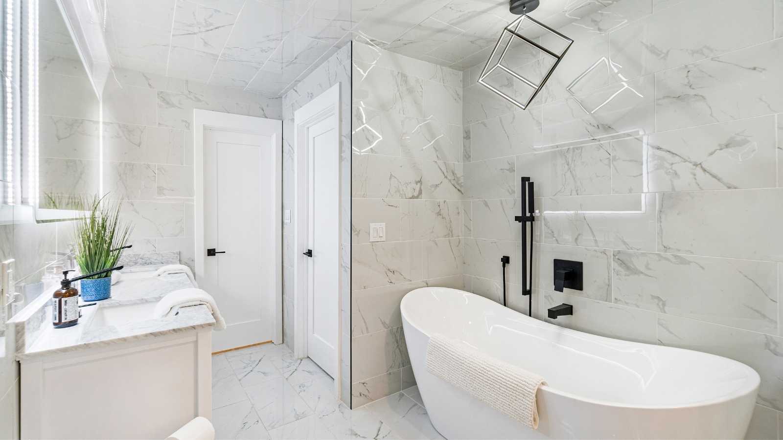 Modern bathroom featuring a freestanding tub, marble tile walls, and a stylish vanity with greenery and sleek fixtures.
