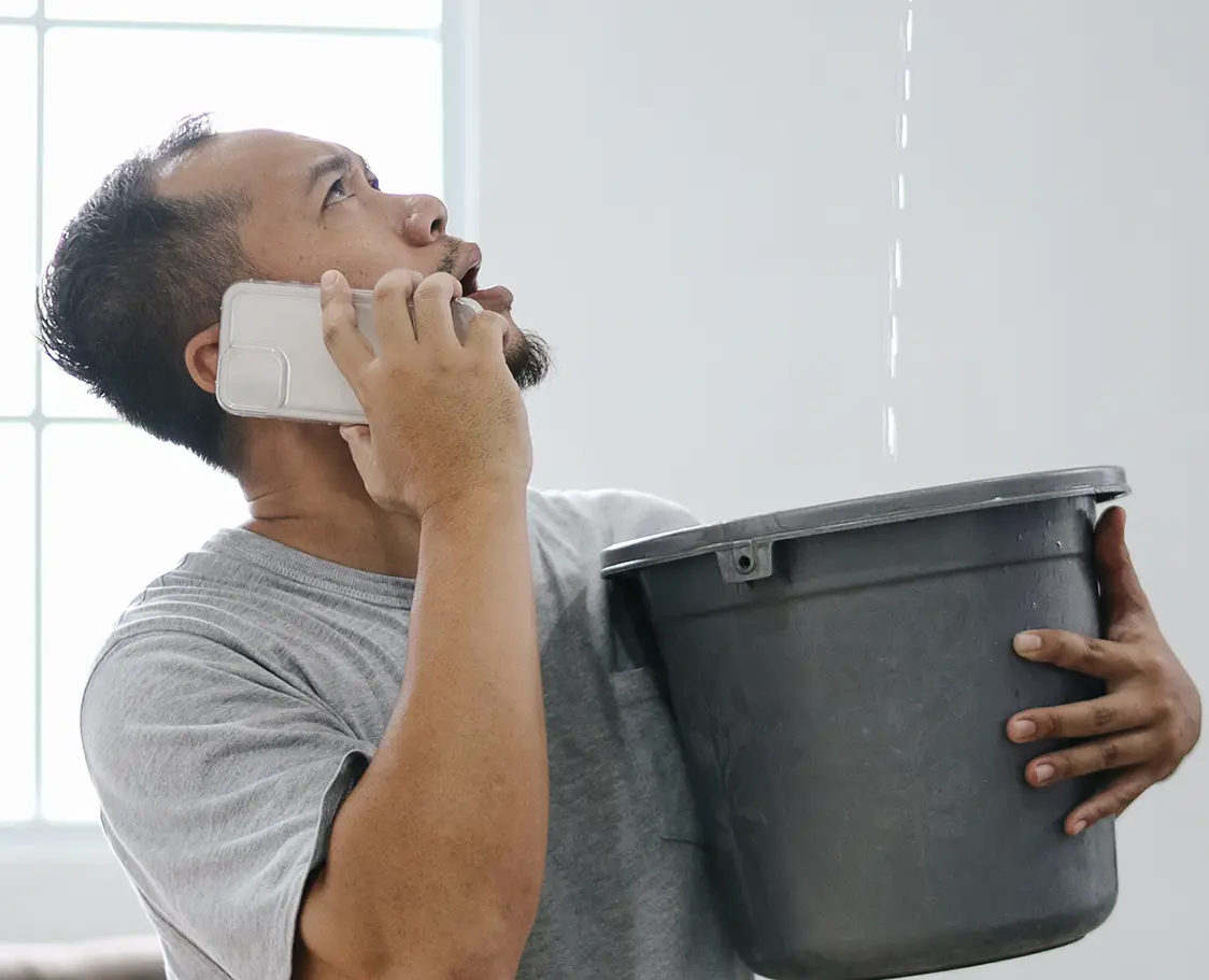 Man catching water in a bucket from a ceiling leak in his home.